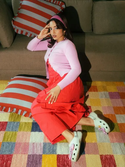 A full-length lifestyle shot for Crocs, showing how the shoes can be styled in a complete, colorful outfit. The overhead angle provides a clear view of the entire look.