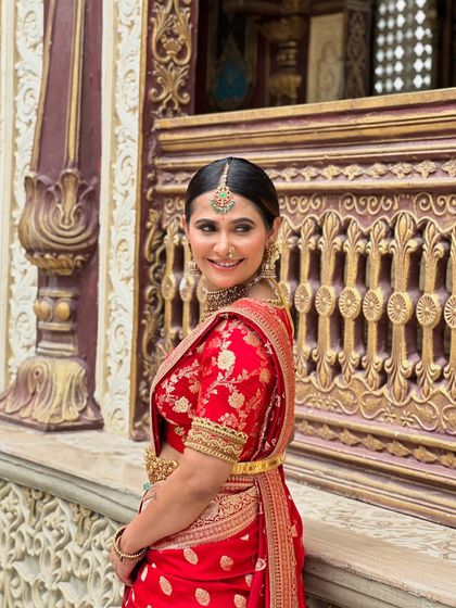 A smiling shot of me in the red Banarasi saree, showcasing the rich color and intricate gold motifs.