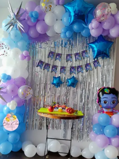 A charming Krishna-themed birthday decoration with a blue and purple balloon arch and a shimmer curtain.