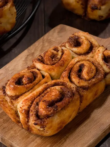A batch of freshly baked cinnamon rolls on a rustic wooden board. The warm lighting and dark background create a cozy, inviting atmosphere.