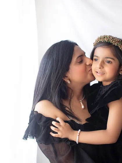 A sweet kiss for her daughter. This candid moment, captured with soft window light, is full of genuine motherly love and affection.