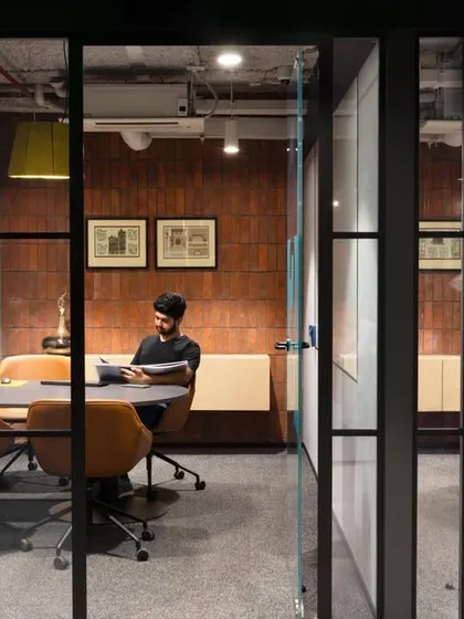 A view into a glass-walled meeting room where a team member is working. The design emphasizes transparency and connectivity.