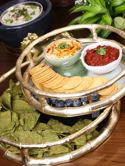 Our two-tiered serving tray with a bamboo-inspired gold frame is perfect for presenting a variety of snacks. Here, it elegantly holds dips, crackers, and fruits, making it a centerpiece for any party.