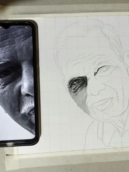 My process begins with precision. Here you can see how I use the grid technique, laying a grid over my paper to match the reference photo on my phone. This method ensures that the proportions and likeness of the final hand-drawn portrait are accurate from the very first line.