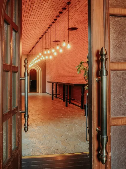 The entrance corridor draws you in with its warm, dramatic lighting and exposed brick. The repetition of pendant lights creates a sense of movement and anticipation, leading guests from the entrance into the main space.