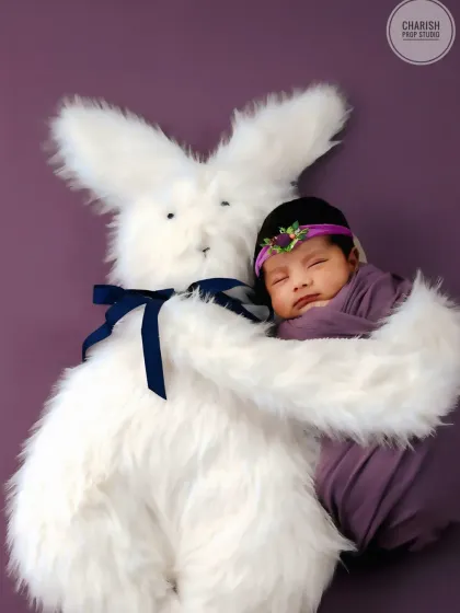 A precious moment as a sleeping newborn is held lovingly in the arms of a big, fluffy bunny prop.