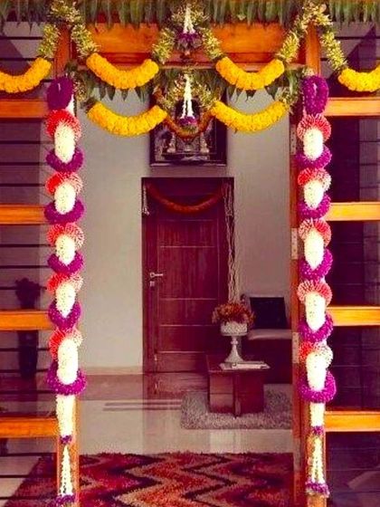 An elegant housewarming flower decoration for a main door. The wooden door is framed with colorful garlands of marigold, jasmine, and purple flowers.