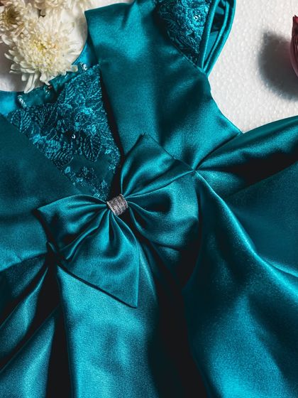 The rich texture of this teal satin dress is enhanced by the intricate lace on the bodice and a beautifully constructed bow. Every element is chosen to create a look of pure luxury.