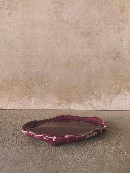 A hand-built plate with a wavy, organic edge, glazed in a deep magenta. This piece is perfect for serving dessert or as a decorative catch-all.