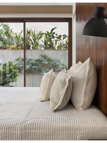 The guest bedroom in the House of Terraces is designed with a minimalist aesthetic. A ribbed wooden headboard and simple, quilted bedding are complemented by a view of the outdoor terrace.