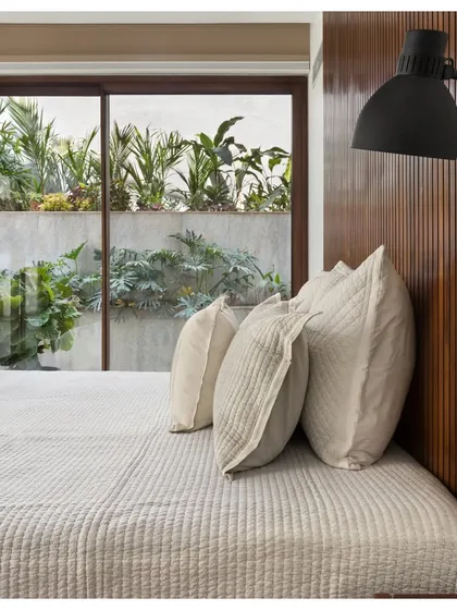 The guest bedroom in the House of Terraces features a minimalist design with a wood-paneled feature wall. A large sliding glass door provides direct access to a tranquil terrace, extending the serene atmosphere outdoors.