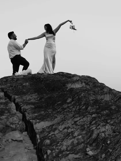 A dramatic black and white shot of the couple on a rocky cliff, conveying a sense of adventure, trust, and epic romance.