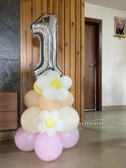A standalone balloon bouquet for a first birthday, featuring a large silver '1' foil balloon on a base of pastel pink, yellow, and cream balloons with small daisy accents.