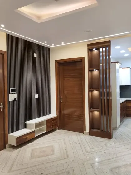 This photo from a recently handed-over project in West Delhi shows the harmony between different spaces, featuring a WPC louvered TV panel, a wooden partition, and a view into the finished kitchen.