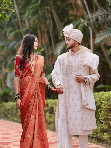 The couple taking a walk, hand in hand. The bride's simple yet elegant orange saree and the groom's classic sherwani make for a beautiful pair.