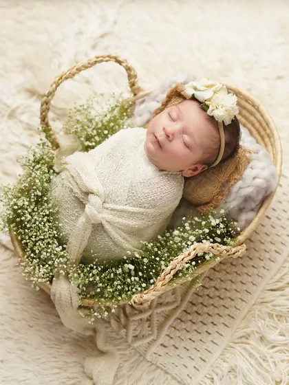 A slightly different angle of the newborn in the floral basket, showing the heart shape of the basket. This is a perfect example of a styled newborn photography setup.