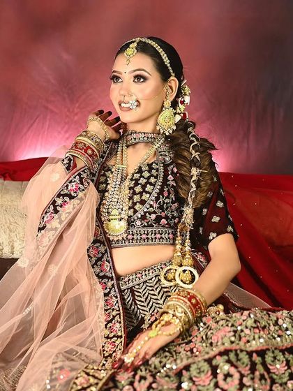 A stunning bridal portrait against a rich red backdrop, highlighting the intricate work on the velvet lehenga.