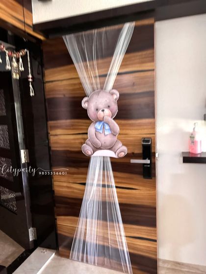 A simple and sweet door decoration to welcome the new baby home, featuring a teddy bear cutout and soft tulle fabric.