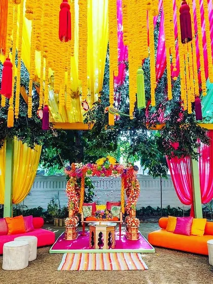 Let's bring the fun to your pre-wedding festivities. This vibrant Mehendi or Sangeet setup is bursting with color, featuring bright fabric drapes, traditional marigold hangings, and comfortable, stylish seating for a day of celebration.