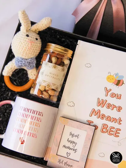 This 'Meant to Bee' themed hamper for a mom-to-be includes a 'Momma' mug, a baby journal, a jar of mixed dry fruits, and a crochet rattle.