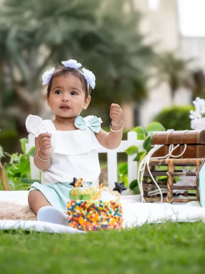 Surrounded by greenery and cute props, this baby girl enjoys her first birthday cake during a lovely outdoor session in a Jaipur park.