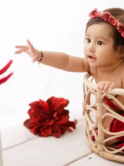 A 6-month-old baby girl curiously reaching for a bright red flower. We use simple props to encourage interaction and capture their natural curiosity.