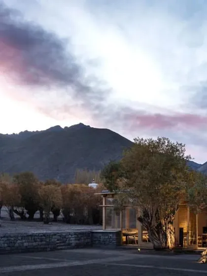 The hotel at dusk, nestled within a grove of willow trees, with the dramatic Himalayan mountains in the background.