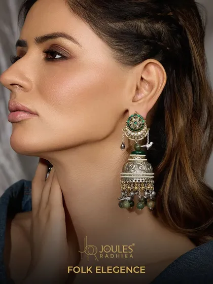 Folk Elegance. These oxidized silver jhumkas feature a delicate bird motif and emerald green drops, combining traditional design with a touch of color.
