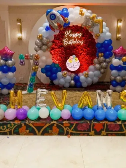 An out-of-this-world astronaut theme for a 7th birthday party. This large-scale setup includes a circular backdrop with a red shimmer panel, balloon pillars, and foil rockets.