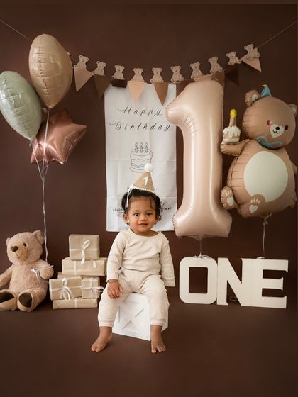 A full view of the charming teddy bear birthday theme, with neutral-colored balloons, a large "1" balloon, and a cute birthday hat on the little one.