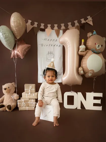 A full view of the charming teddy bear birthday theme, with neutral-colored balloons, a large "1" balloon, and a cute birthday hat on the little one.
