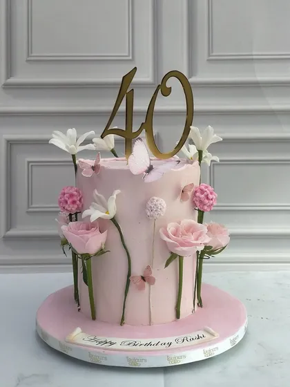 A sophisticated cake for a 40th birthday. The soft pink tier is decorated with delicate, individually placed sugar flowers and butterflies, creating the look of a whimsical garden growing up the side of the cake.