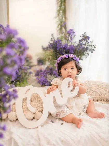 A floral fantasy for a first birthday. This little girl is holding a "One" sign, surrounded by a cascade of beautiful purple flowers.