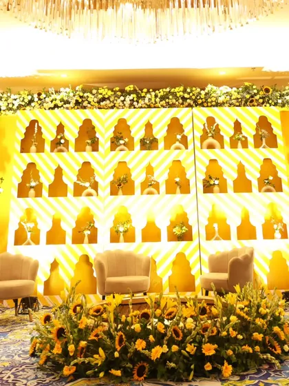 A wider view of the Haldi stage, showcasing the plush seating for the couple, framed by a bed of fresh sunflowers and a beautifully illuminated backdrop.