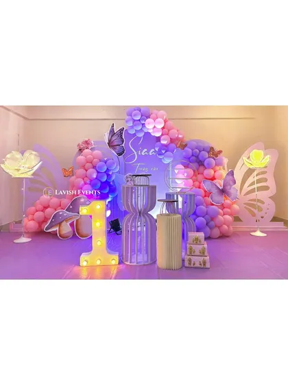 An enchanting butterfly-themed party with purple and pink lighting, large glowing butterfly wing props, and a light-up number '1' for a magical first birthday.