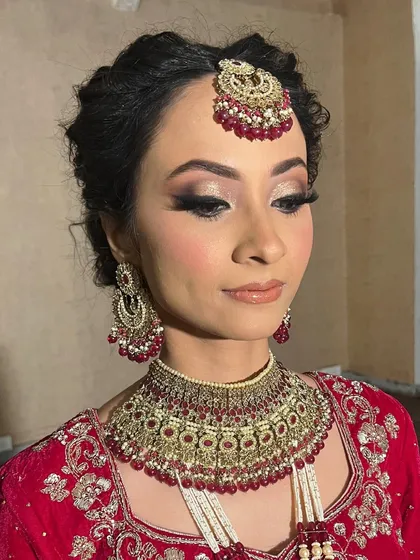 A classic bridal glam look featuring soft, shimmering eyeshadow and defined lashes. The intricate updo and traditional red jewelry complete this elegant wedding day style.