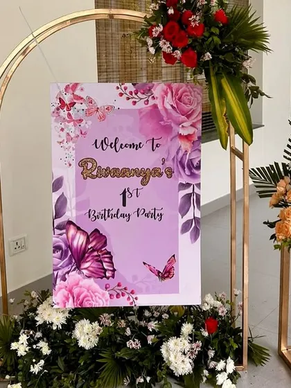 A floral and butterfly themed welcome sign for a first birthday party, framed by a golden arch and fresh flower arrangements for an elegant entrance.