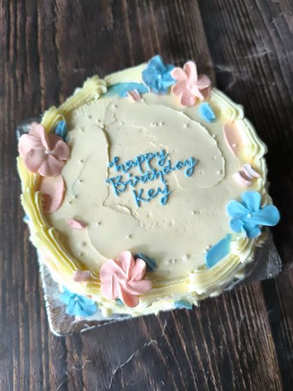 A shabby chic floral cake with a rustic, textured finish. The pink and blue buttercream flowers give it a soft, whimsical feel.
