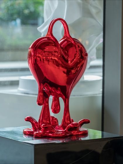 The full "Melting Affection" sculpture, its vibrant red form a stark and beautiful contrast against the gallery window.