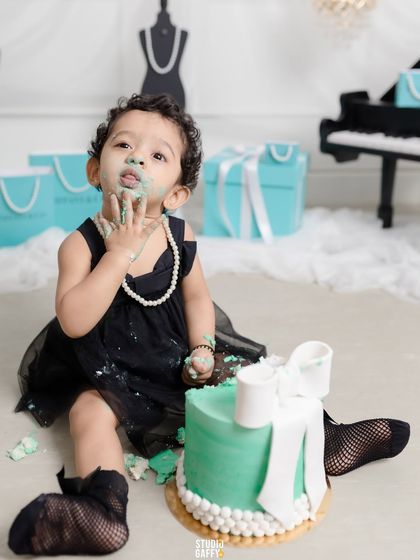 A "Breakfast at Tiffany's" themed cake smash, where this little lady is enjoying her cake with pearls and style. It's a perfect example of a chic and fun first birthday shoot.