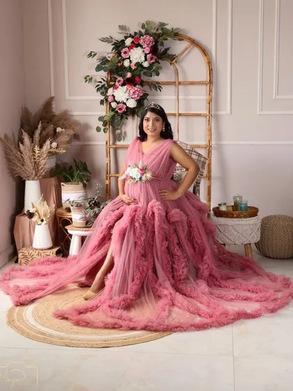 A stunning full-length portrait in a pink ruffled gown, showcasing the beauty of the dress and the radiant mama-to-be in the boho setup.