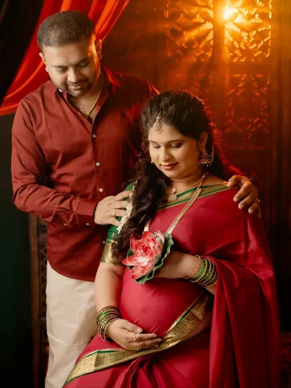 A tender moment between a couple during their traditional maternity shoot. The partner's hand rests protectively on her shoulder as she holds a lotus flower.