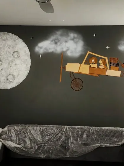 We created this custom mixed-media mural for a child's bedroom. The piece combines a hand-painted night sky with a textured moon and a 3D airplane element crafted from different shades of wood cutouts.
