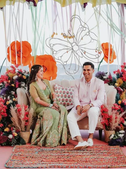 A colorful and artistic Mehendi seating area, featuring large paper flowers, vibrant floral arrangements, and bohemian-style rugs, creating a cheerful and relaxed atmosphere.