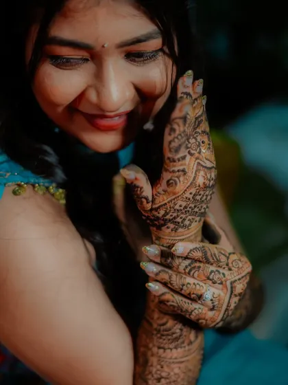 A close up shot capturing the bride's smile as she admires the intricate patterns of her bridal mehndi.