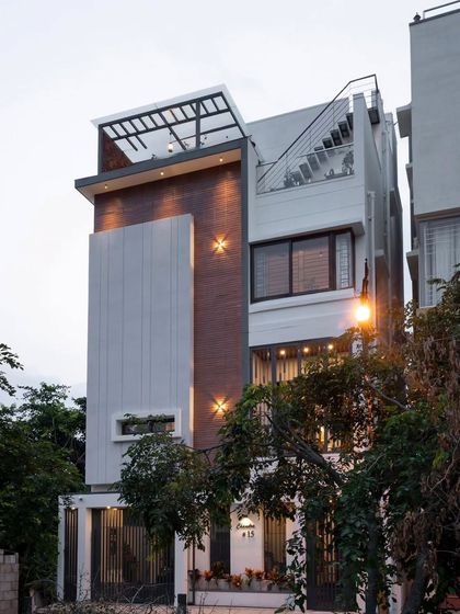 The completed facade of our Banashankari 6th Stage project, a home designed for a compact plot. The elevation features warm brick cladding against soft grey textured walls with vertical grooves, creating a clean, contemporary look.