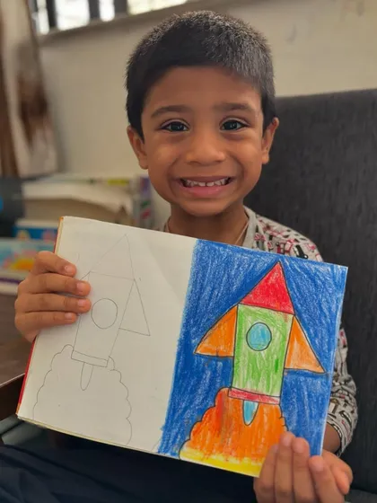 3, 2, 1, blast off! A junior KG student proudly presents his rocket ship drawing. This activity is great for teaching simple geometric shapes and encouraging imaginative play through art.