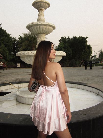 The back view of the pink babydoll dress near a fountain.