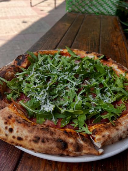 Our Parma Ham & Arugula pizza on an outdoor table. It's the perfect companion for a sunny afternoon.