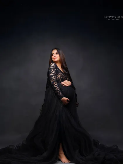 A full-length portrait in a dramatic black lace and tulle gown. This shot highlights the elegant silhouette of the mother-to-be against a classic dark backdrop.